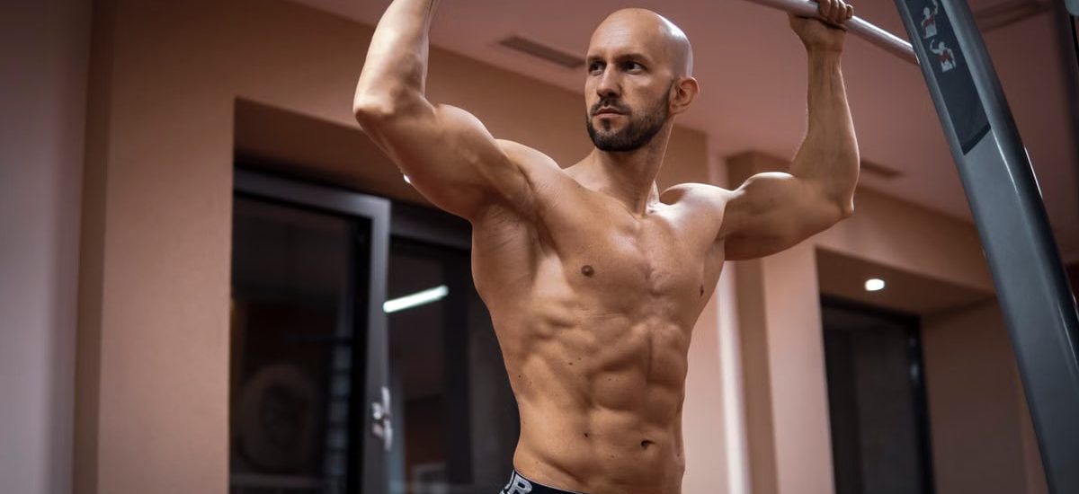 A bald, muscular man performing exercise on gym equipment indoors.